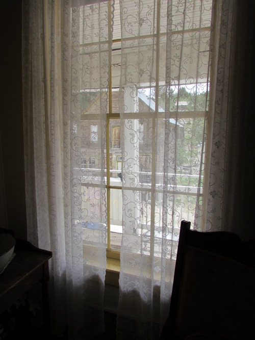 Kristin Holt | Historic Idaho Hotel in Silver City. View from the inside of room 7 (upper far-left window when viewed from the street). Notice the wooden structure across the street as viewed through the lace curtains and historic window panes.