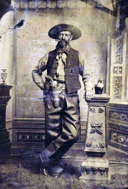 Kristin Holt | Armed Gunmen: Holsters, Braces, and Scabbards. COWBOY WITH COLT SINGLE ACTION ARMY - ca.1875-1890. A wonderfully expressive tintype portrait of a rough Cowboy chomping on his cigar, featuring a nickel-plated Colt Single Action Army and holster rig. The cowboy has pulled the Colt "Peacemaker" out of the holster and turned it around so that it faces outward. He is wearing leather chaps, a bandana, a hat, vest and boots. There is a whiskey bottle next to him on the pedestal. A great original tintype image of an iconic Western cowboy. Image: Courtesy of Pinterest.