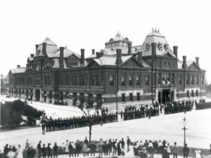Pullman strikers outside Arcade Building in Pullman, Chicago. The Illinois National Guard can be seen guarding the building during the Pullman Railroad Strike in 1894. Image: Public Domain, courtesy of Wikipedia