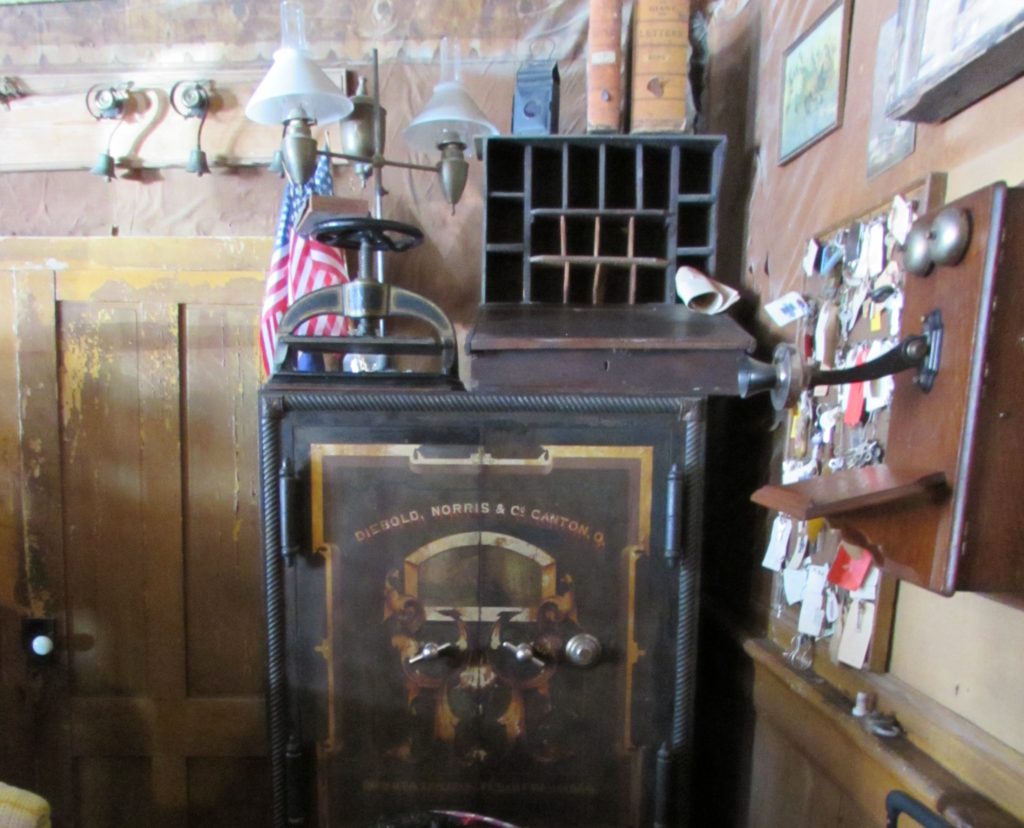 Kristin Holt | Historic Idaho Hotel in Silver City. Antique safe behind the Check-In desk at Idaho Hotel, Silver City, Idaho. Note the bells above the door (top left), the vintage telephone (far right), and the writing desk (lap or tabletop use) on top of the safe. Vintage stationery from a prominent female guest had been found in the desk in this century. See the dual oil lamps and message boxes behind the lap desk (also on top of safe). The lobby is filled with antique treasures!