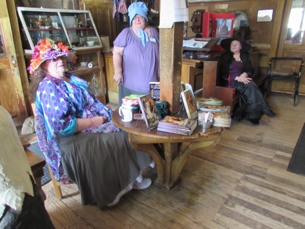 Kristin Holt | Historic Idaho Hotel in Silver City. Jacquie Rogers (seated, left) at an unusual and clever antique table, built around a support beam in the lobby of historic Idaho Hotel (Silver City, Idaho). Jacquie Rogers held a book signing during her Much Ado About Silver City event in June, 2016.