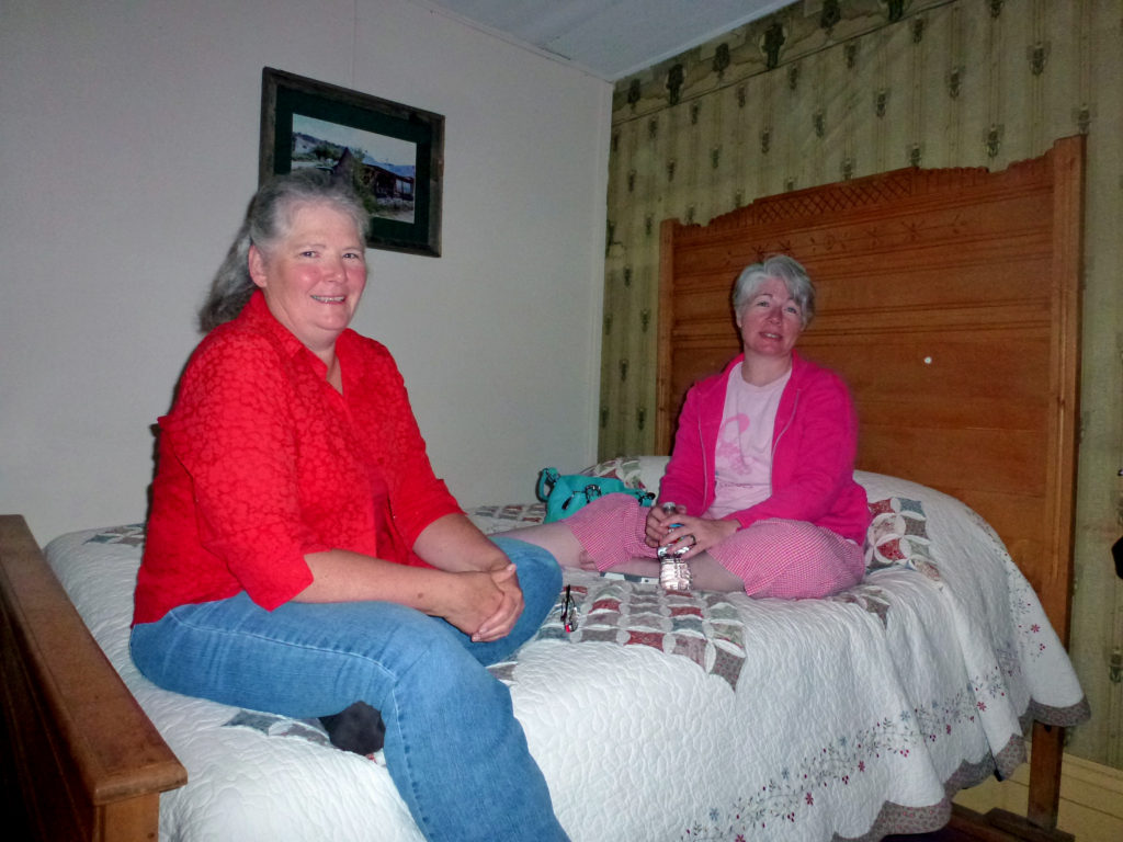 Kristin Holt | Historic Idaho Hotel in Silver City. Authors Paty Jager (left) and Kristin Holt (right) visiting late one evening in Shirl Deems's room at the historic Idaho Hotel, Silver City, Idaho. Note the antique bed frame and vintage wallpaper. Image courtesy of Shirl Deems.