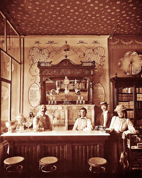 Kristin Holt | The Victorian-era Soda Fountain. Black and white vintage photograph: Soda fountain with soda men behind the bar. Image Courtesy of Pinterest.