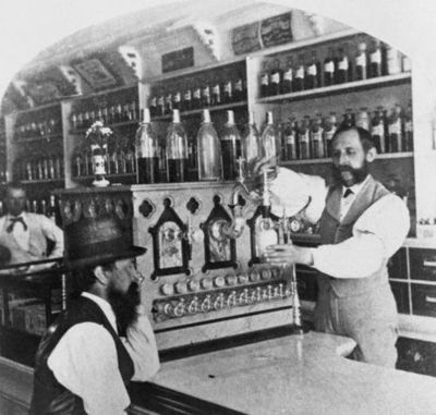 Kristin Holt | The Victorian-era Soda Fountain. Black and white vintage photograph: Worker pouring soda for a customer, circa 1890. Image Courtesy of Pinterest.