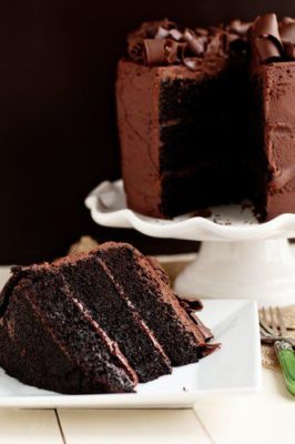 Kristin Holt | Victorian Baking: Devil's Food Cake ~ photograph of restaurant-style three-layer dark chocolate cake. Plated slice, with remaining cake on pedistal in background. Image copyright freepik; subscription use.